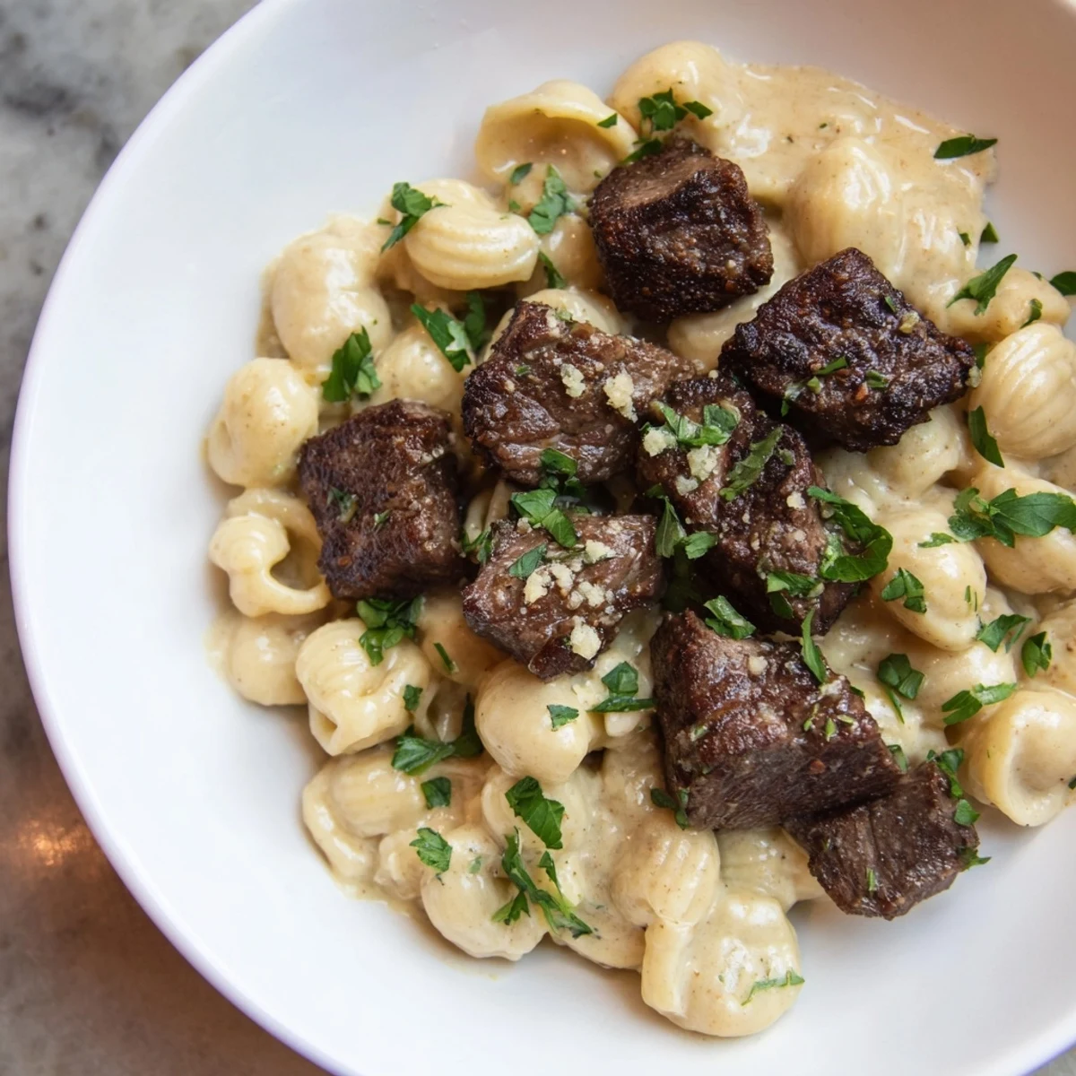 Garlic butter steak bites glistening from the skillet, served atop creamy cheesy pasta shells.