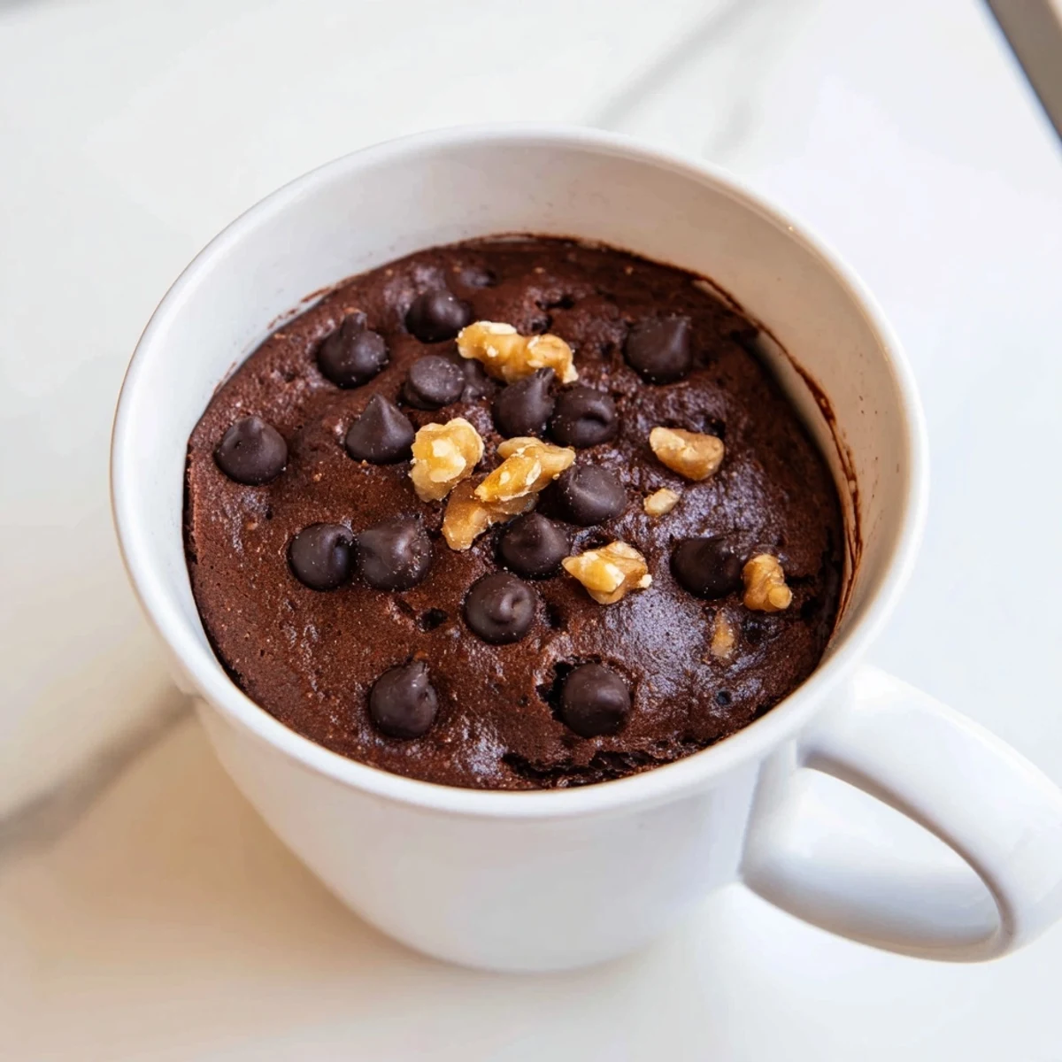 Steaming-hot chocolate Microwave Mug Cake topped with chocolate chips, ideal for a sweet treat.