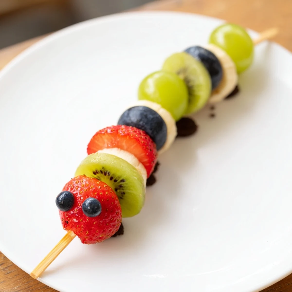Vibrant Caterpillar Fruit Skewer Track, a kid-friendly treat with colorful, skewered fruit and cookie crumbs.