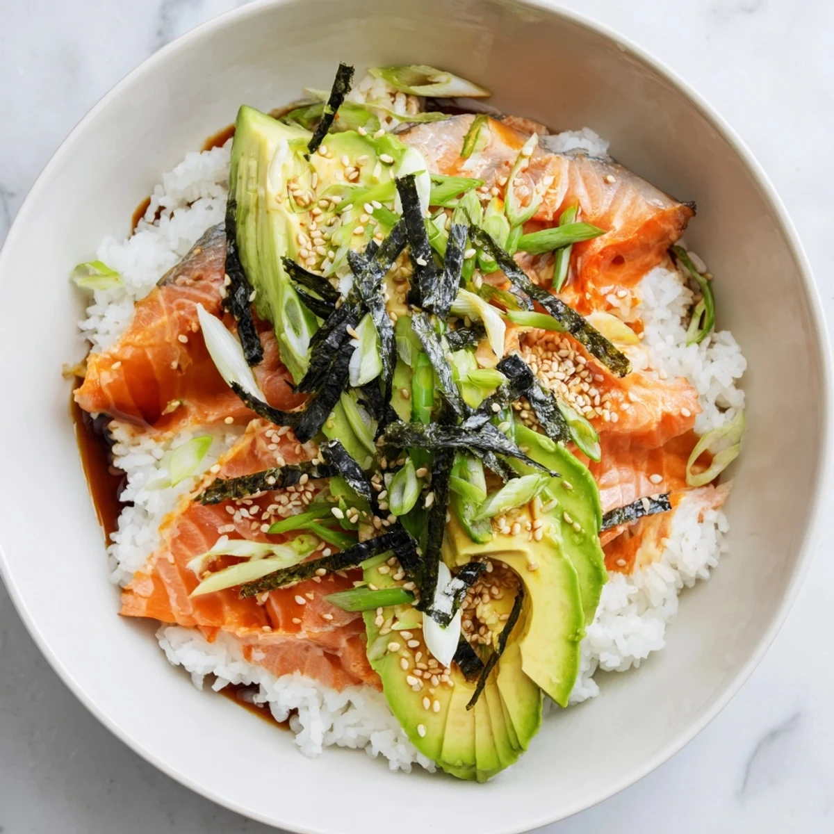 Flaky salmon rice bowl, perfectly seasoned and topped with creamy avocado, sesame seeds, and green onions.