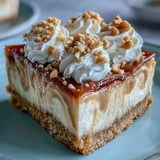 A perfectly sliced piece of Nutter Butter cheesecake on a white plate, topped with a dollop of whipped cream and chopped peanuts.