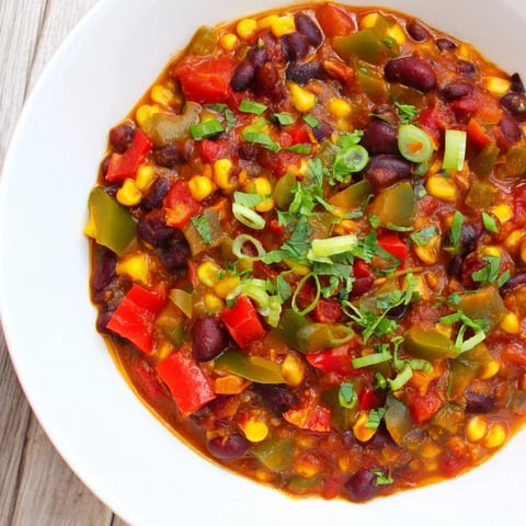 Steaming veggie chili, vibrant with beans and veggies, served in a rustic bowl with toppings.