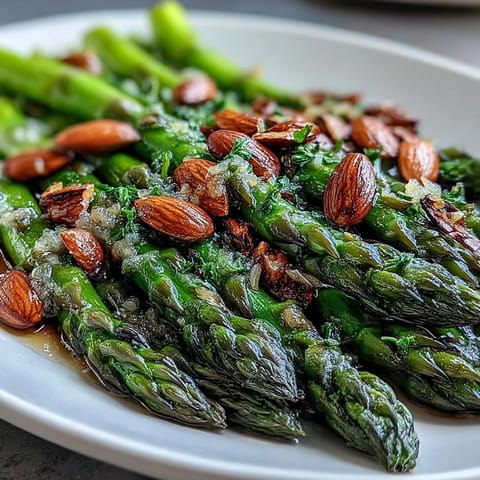 A vibrant plate of lemon butter asparagus with almonds, showcasing bright green spears glistening in citrusy butter and topped with golden toasted nuts.