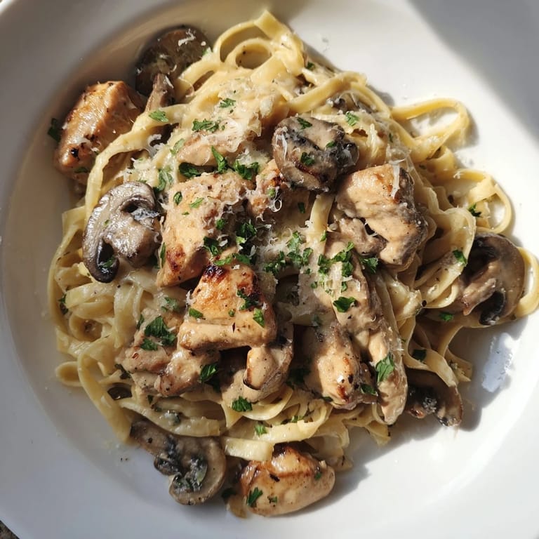 A close-up of creamy mushroom chicken pasta, rich sauce coating fettuccine and tender chicken.